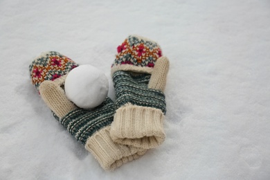 Photo of Knitted mittens and snowball on snow outdoors