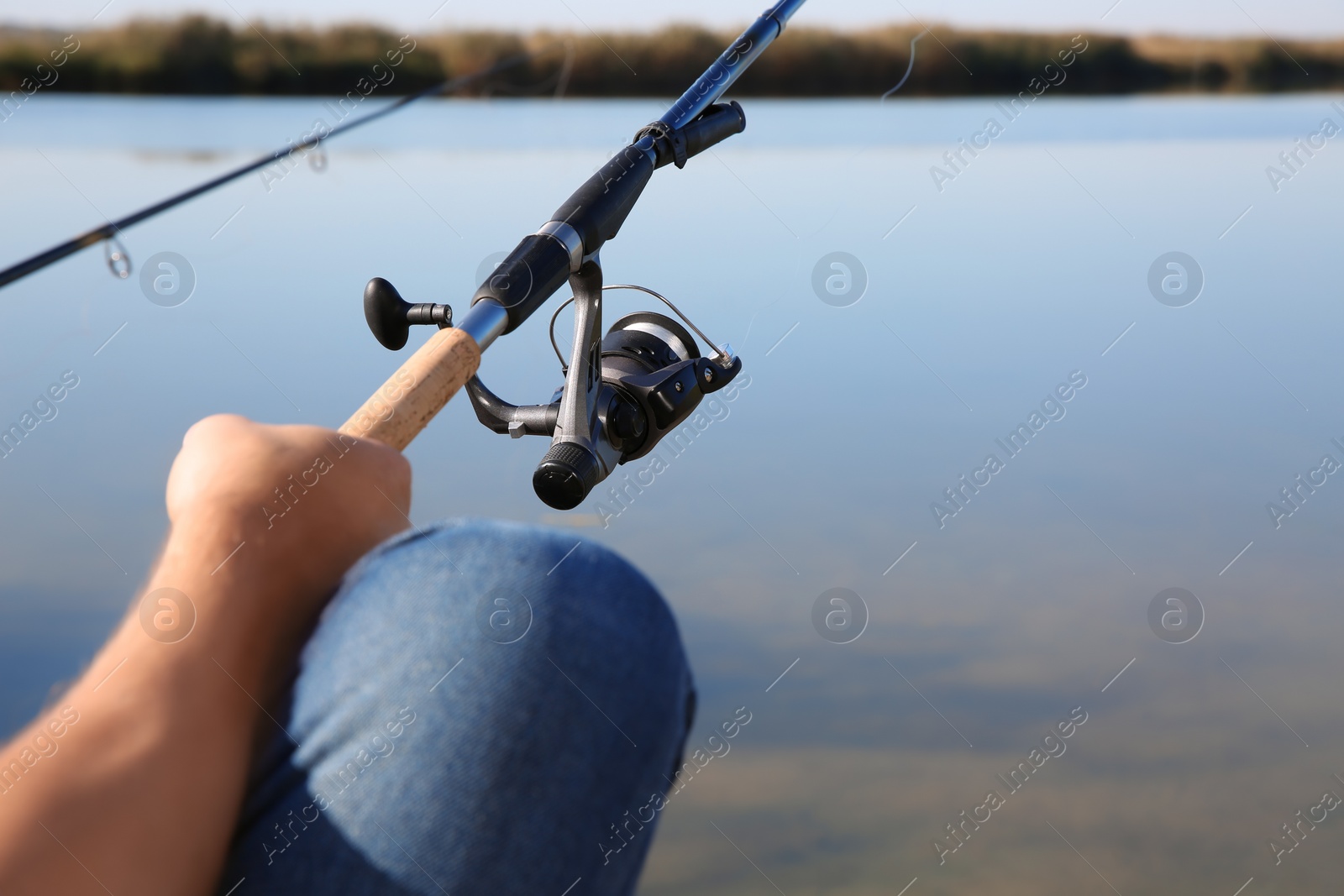 Photo of Man fishing alone at riverside on sunny day, closeup