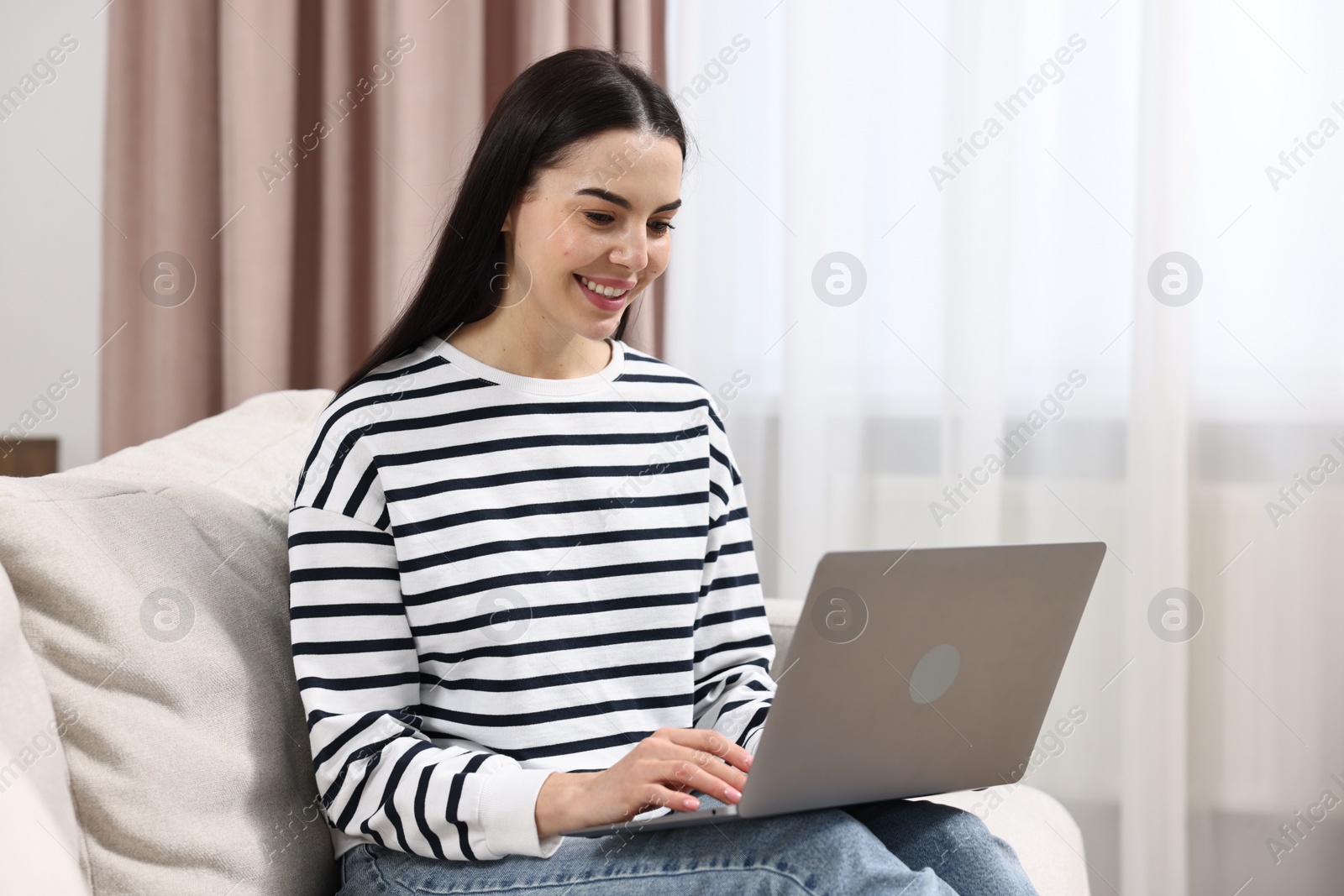 Photo of Happy young woman using laptop on sofa at home