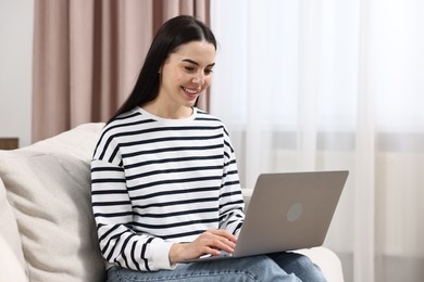 Photo of Happy young woman using laptop on sofa at home