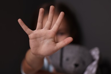 Photo of Child abuse. Little girl with toy bunny doing stop gesture on dark background, selective focus