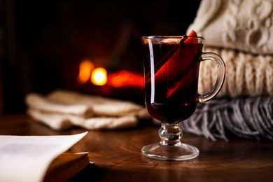 Photo of Tasty mulled wine, book, knitwear and blurred fireplace on background