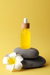 Photo of Bottle of face serum, spa stones and beautiful flower on yellow background