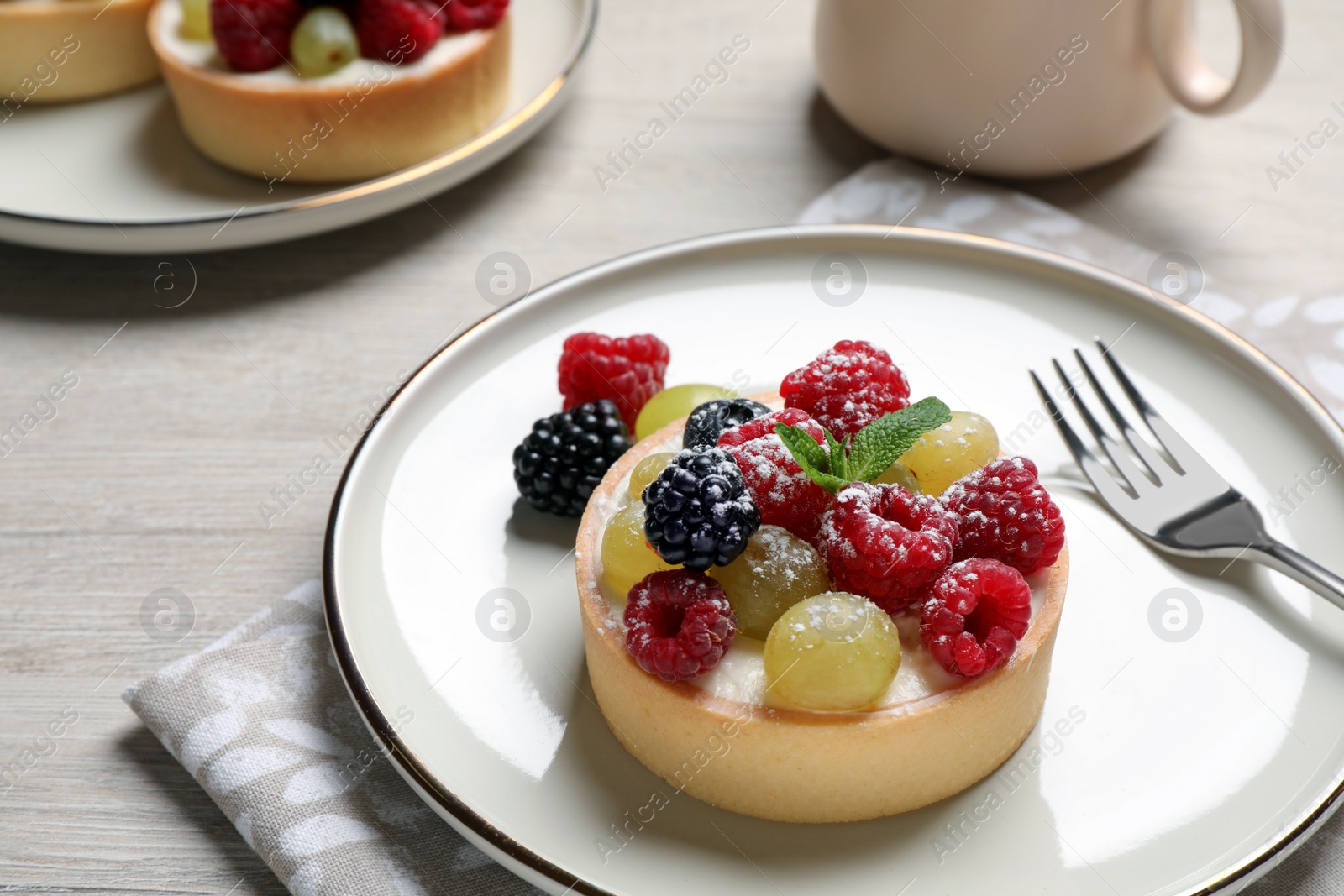 Photo of Delicious tartlet with berries on light wooden table