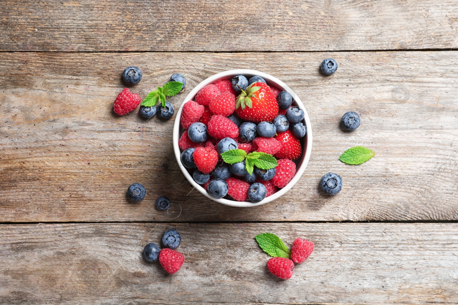 Photo of Bowl with raspberries, strawberries and blueberries on wooden table, top view