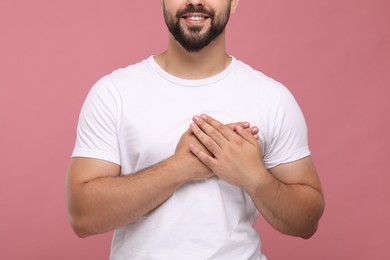 Photo of Thank you gesture. Grateful man holding hands near heart pink background, closeup