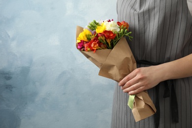 Photo of Woman holding bouquet with beautiful freesia flowers on color background, closeup. Space for text