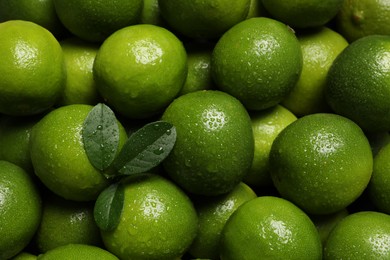 Photo of Fresh ripe limes and leaves with water drops as background, top view