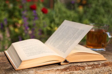 Open book with glass cup of tea on wooden table in garden, closeup