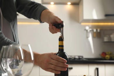 Man opening wine bottle with corkscrew indoors, closeup. Space for text