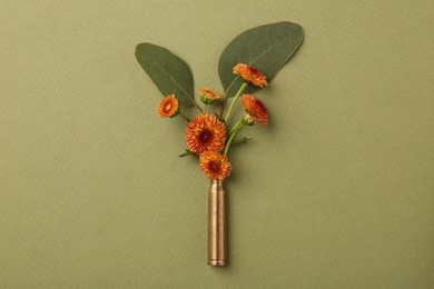 Beautiful flowers in bullet case on green background, top view