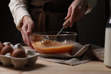 Photo of Woman whisking eggs in bowl at table, closeup