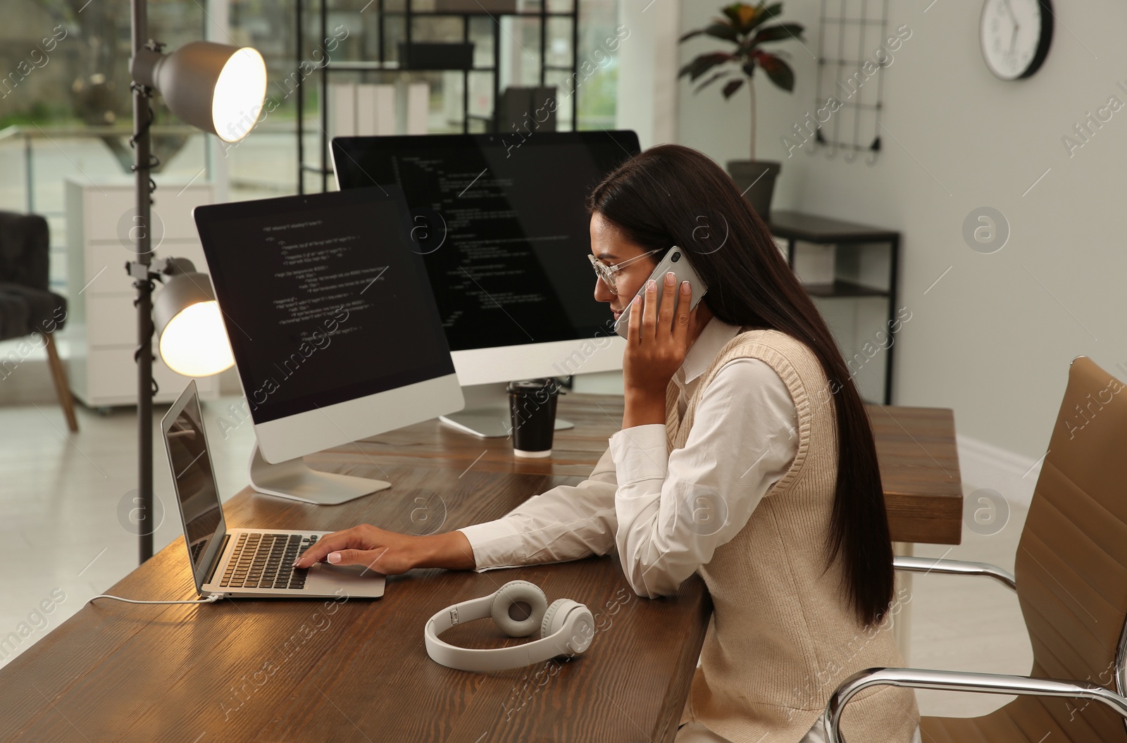 Photo of Programmer talking on phone while working at desk in office