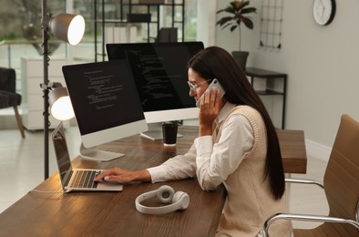 Photo of Programmer talking on phone while working at desk in office