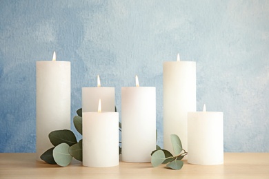 Composition with burning candles on table against color background