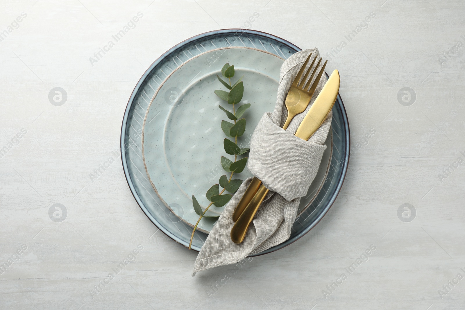 Photo of Stylish setting with cutlery, napkin, eucalyptus branch and plates on white table, top view