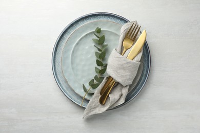 Photo of Stylish setting with cutlery, napkin, eucalyptus branch and plates on white table, top view