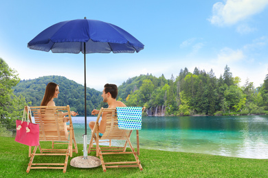 Image of Young couple relaxing on sun loungers near river and mountains. Luxury vacation 