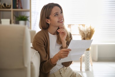 Photo of Happy woman reading letter near sofa at home