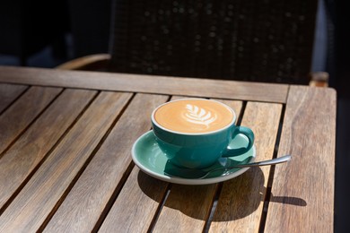 Cup of aromatic hot coffee and spoon on wooden table in outdoor cafe, space for text