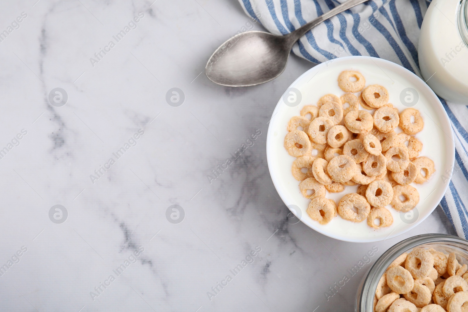 Photo of Breakfast cereal. Tasty corn rings, milk and spoon on white marble table, top view. Space for text