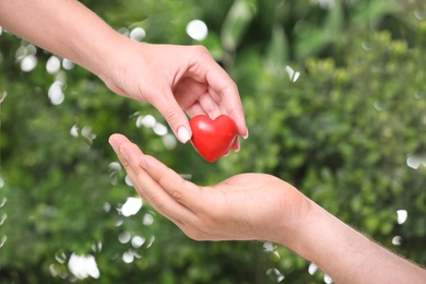 Photo of Woman giving red heart to man on blurred green background, closeup. Donation concept
