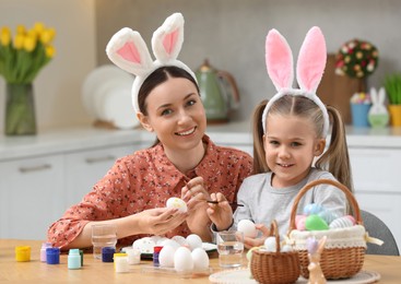 Mother and her cute daughter painting Easter eggs at table in kitchen