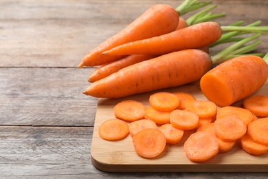 Photo of Board with fresh and cut carrots on wooden background. Space for text