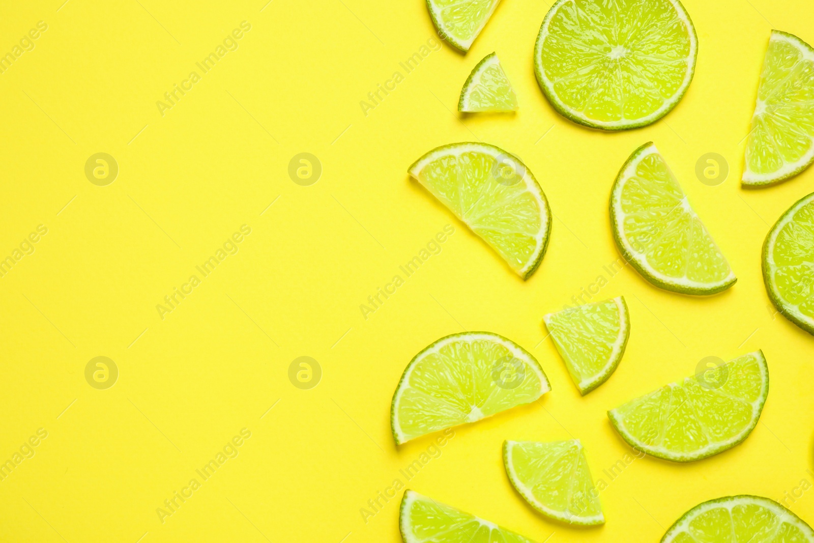 Photo of Juicy fresh lime slices on yellow background, flat lay. Space for text
