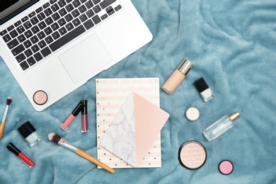 Flat lay composition with laptop, notebook and makeup products for woman on fabric