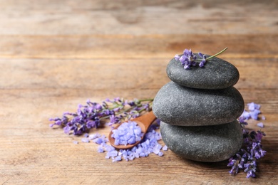 Photo of Spa stones, natural cosmetic bath salt and lavender flowers on wooden table, space for text