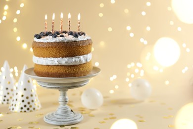Photo of Tasty cake with burning candles on beige background against blurred lights. Space for text