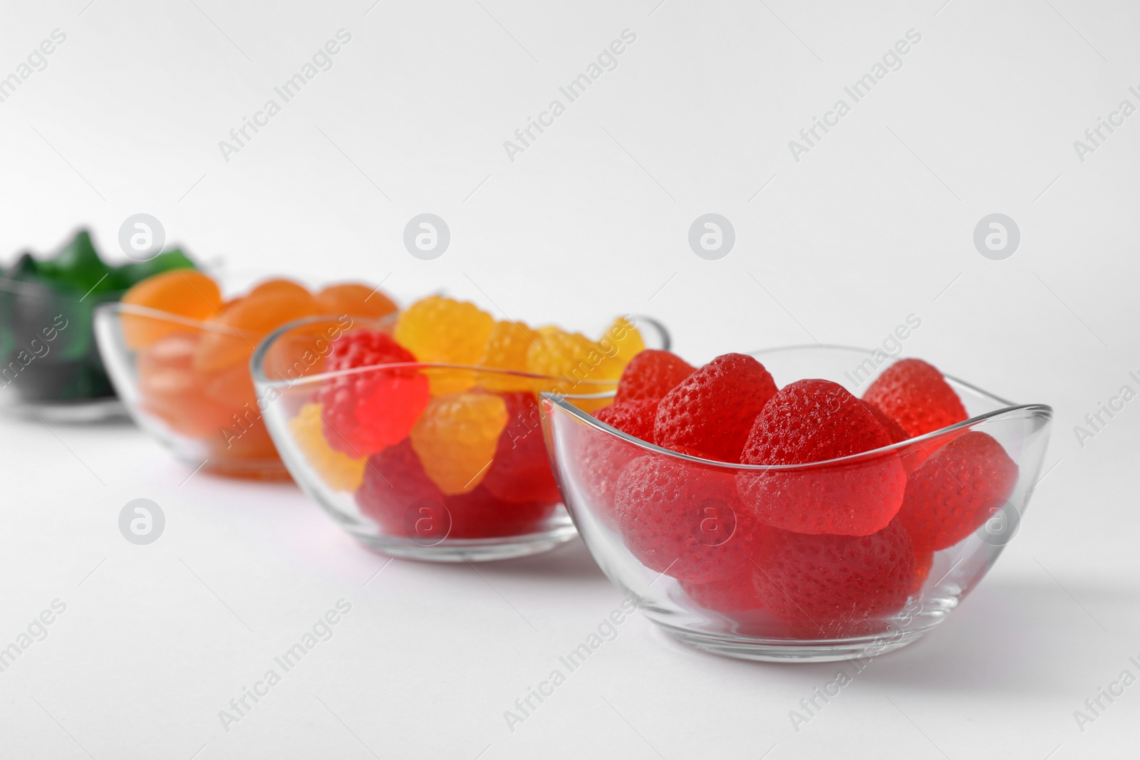 Photo of Different delicious gummy candies in bowls on white background, closeup