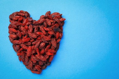 Photo of Heart shaped pile of dried goji berries on light blue background, top view. Space for text