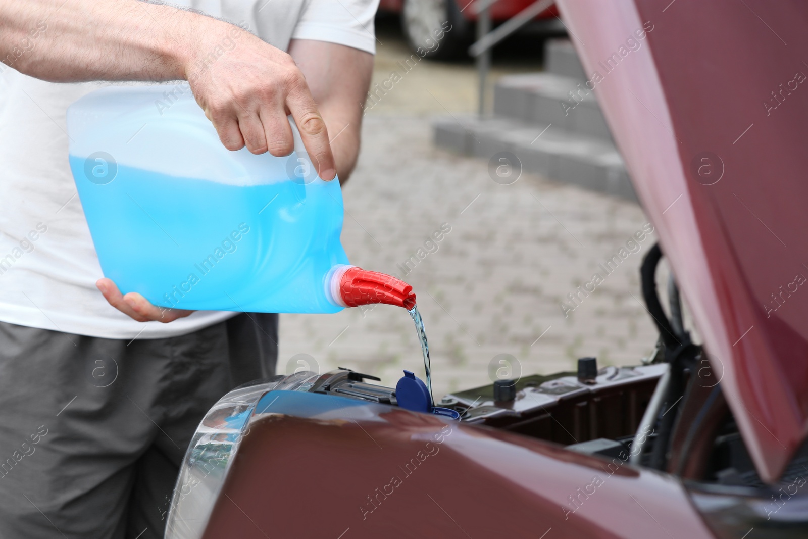 Photo of Man pouring liquid from plastic canister into car washer fluid reservoir, closeup