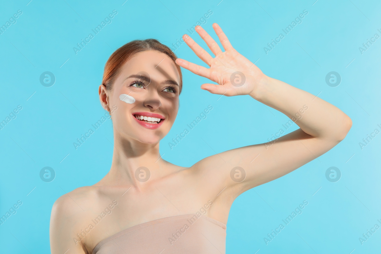 Photo of Beautiful young woman shading herself with hand from sunlight on light blue background