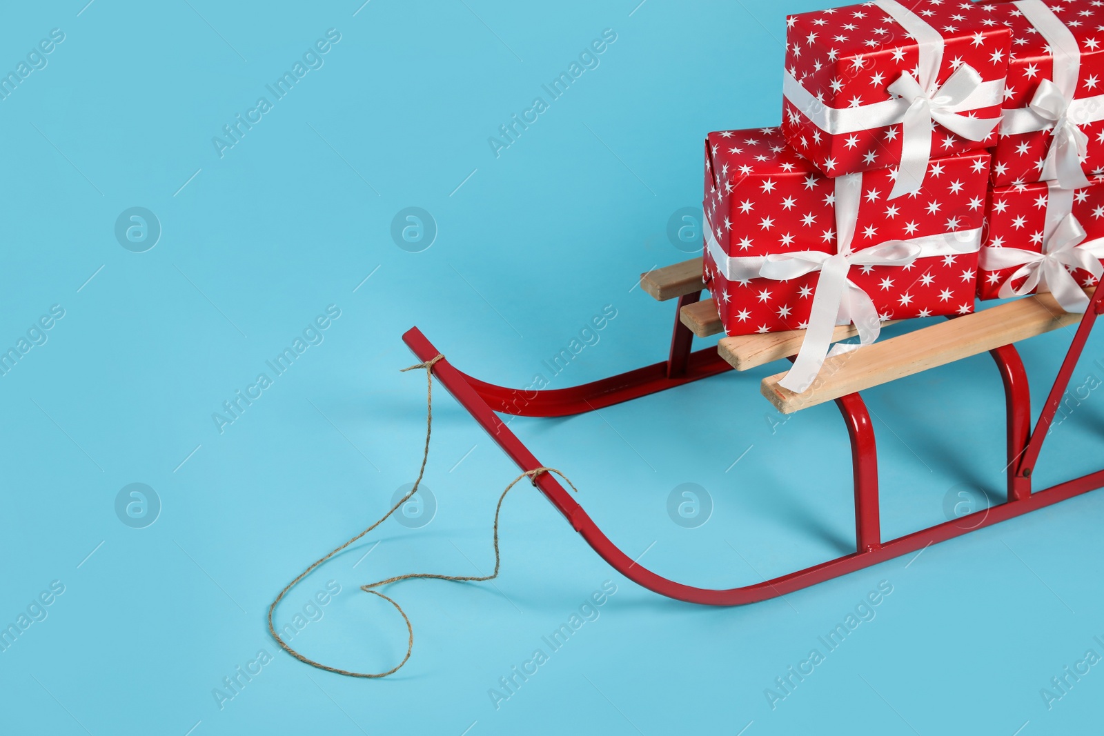 Photo of Stylish sleigh with Christmas gifts on light blue background, space for text