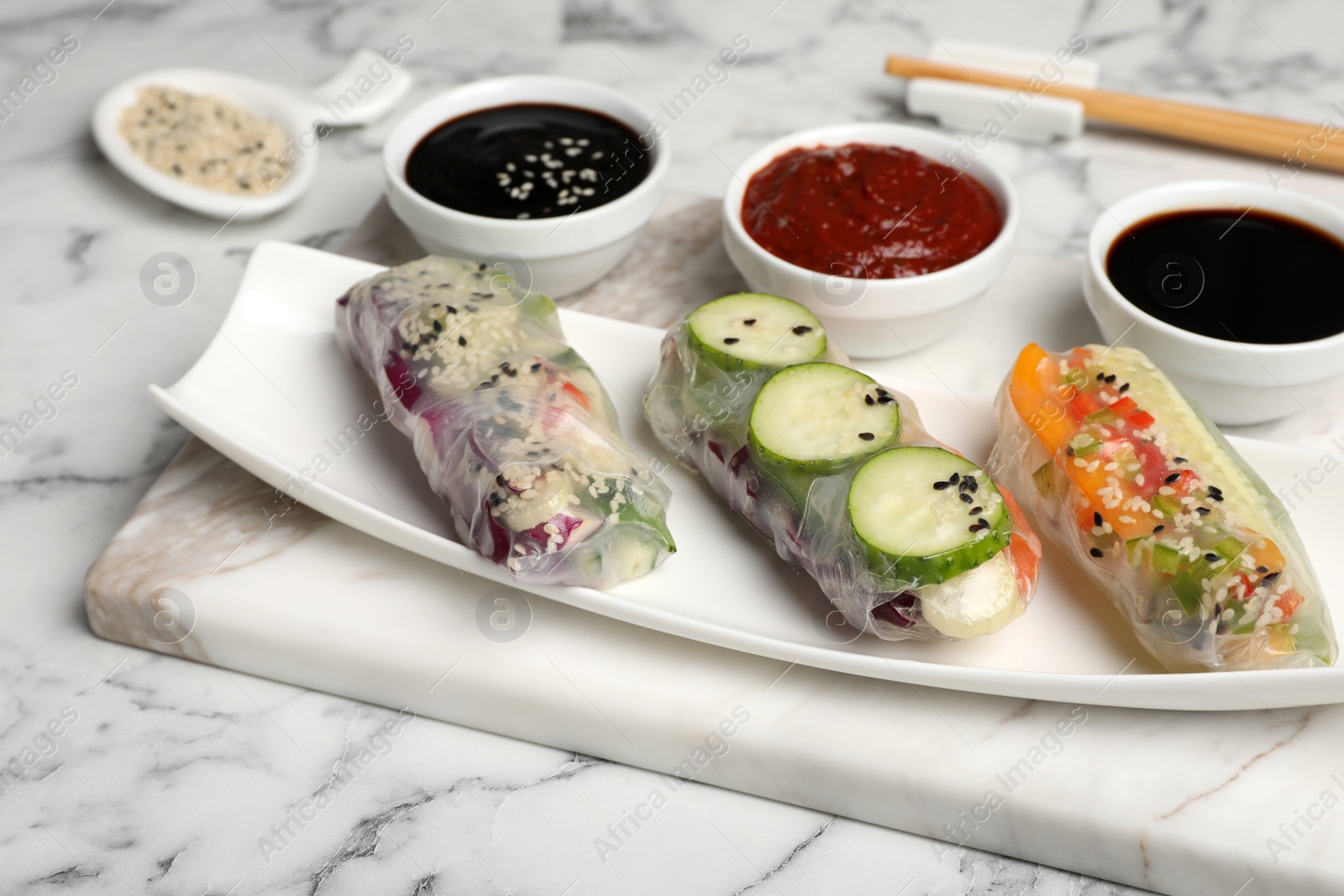 Photo of Different delicious rolls wrapped in rice paper on white marble table