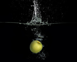Photo of Ripe apple falling down into clear water with splashes against black background
