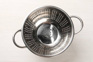 Metal colander on white wooden table, top view