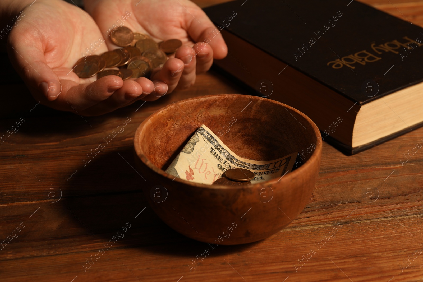 Photo of Donate and give concept. Woman holding coins, closeup. Bible and bowl of money on wooden table