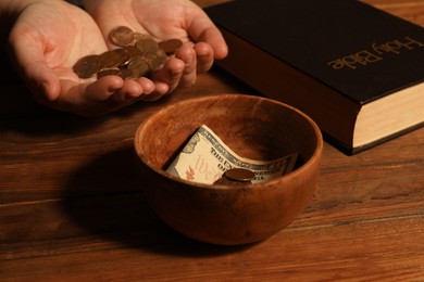 Photo of Donate and give concept. Woman holding coins, closeup. Bible and bowl of money on wooden table