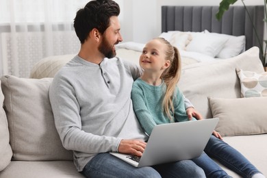 Happy man and his daughter with laptop on sofa at home