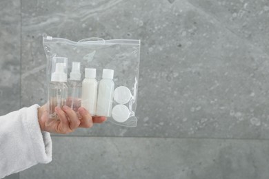 Woman holding plastic bag of cosmetic travel kit near grey wall, closeup and space for text. Bath accessories