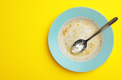 Photo of Dirty plate with food leftovers and spoon on yellow background, top view. Space for text