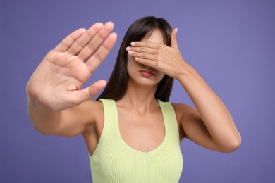 Photo of Embarrassed woman covering face on violet background
