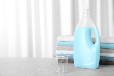 Photo of Measuring cup near bottle of laundry detergent and stacked towels on table. Space for text