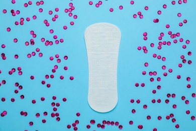Photo of Sanitary pad and pink sequins on light blue background, flat lay. Menstrual cycle
