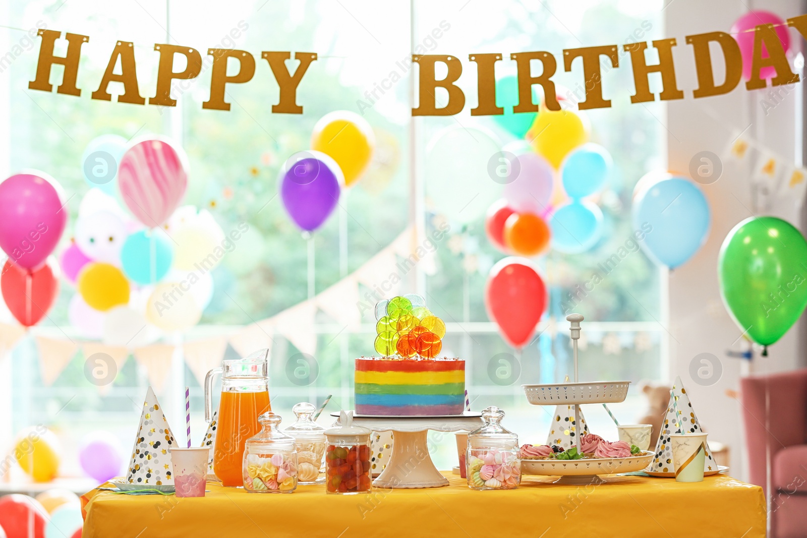 Photo of Bright birthday cake and other treats on table in decorated room