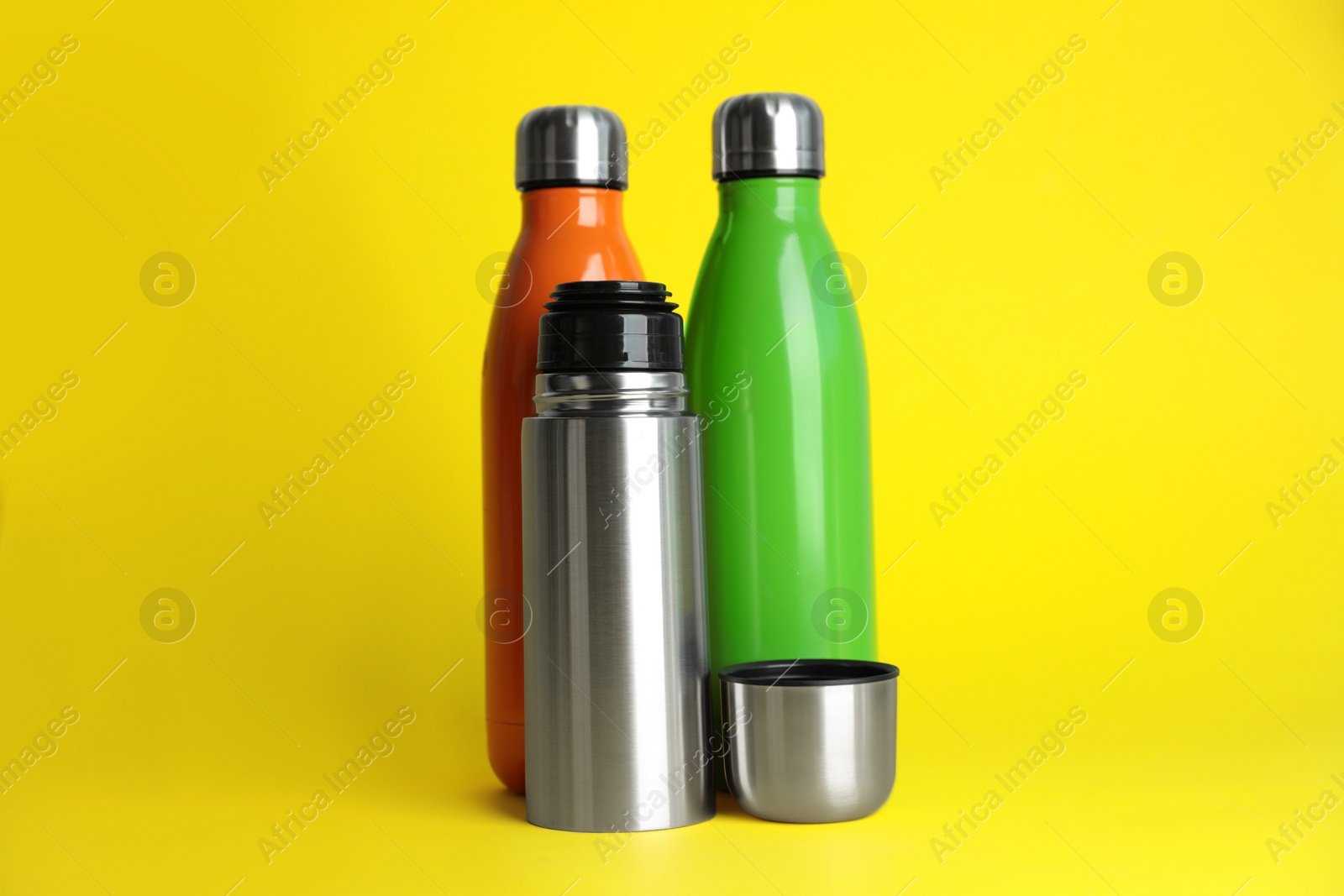 Photo of Stylish stainless thermo bottles on yellow background